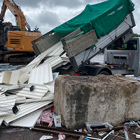 Green dump truck unloading construction debris at recycling site